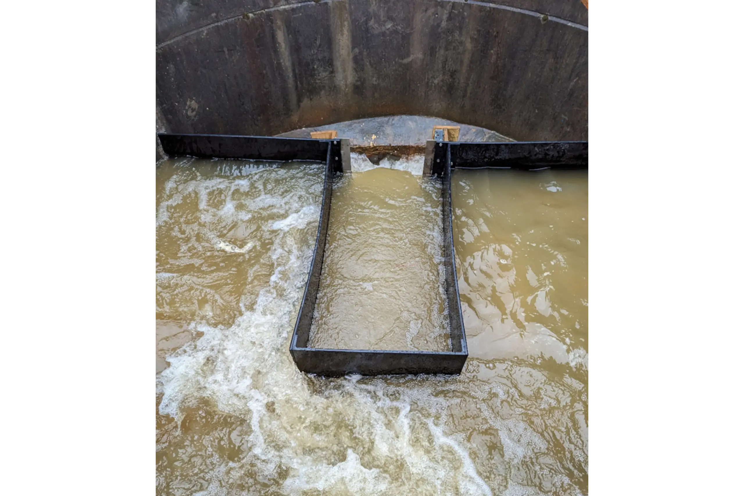 Image of the flow entering through the 300mm pipes causing turbulence, which previously drowned the flume, which is now calmed by the newly installed baffle arrangement. The rectangular weir can be seen towards the outlet of the chamber.