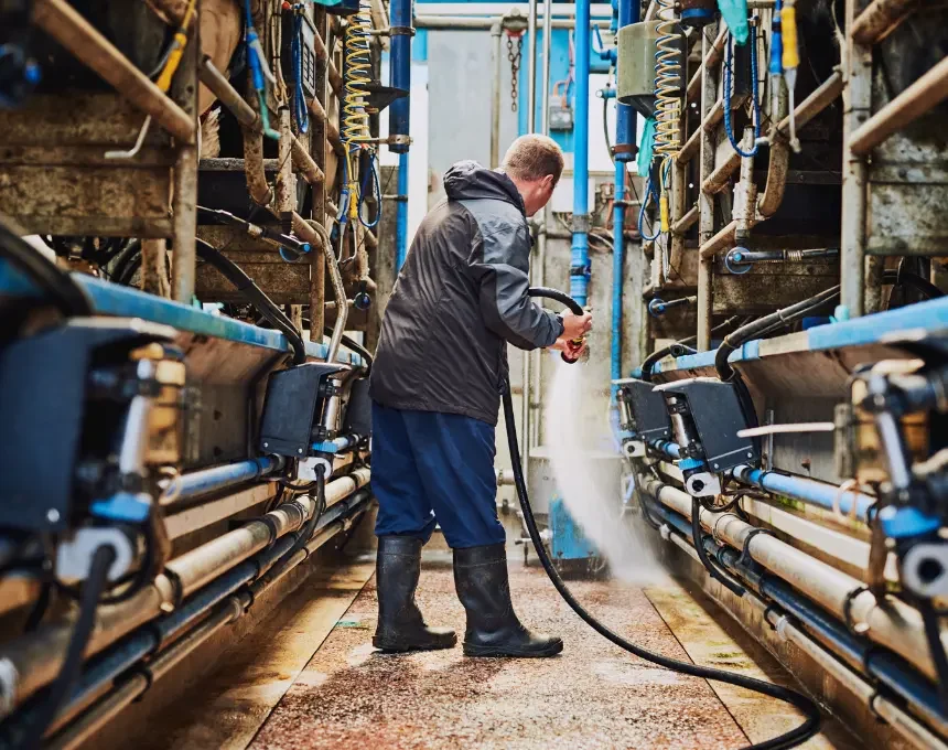 Male farmer hosing off the floor inside a dairy factory